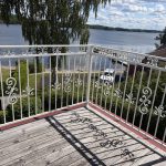 Vitt balkongräcke i smide modell B7c, varmförzinkat och pulverlackerat i RAL 9010. Specialtillverkat, monterat i Rimforsa. Balkongräcke i smide modell B7c i vit RAL 9010 med sjöutsikt, varmförzinkat och pulverlackerat i Rimforsa.